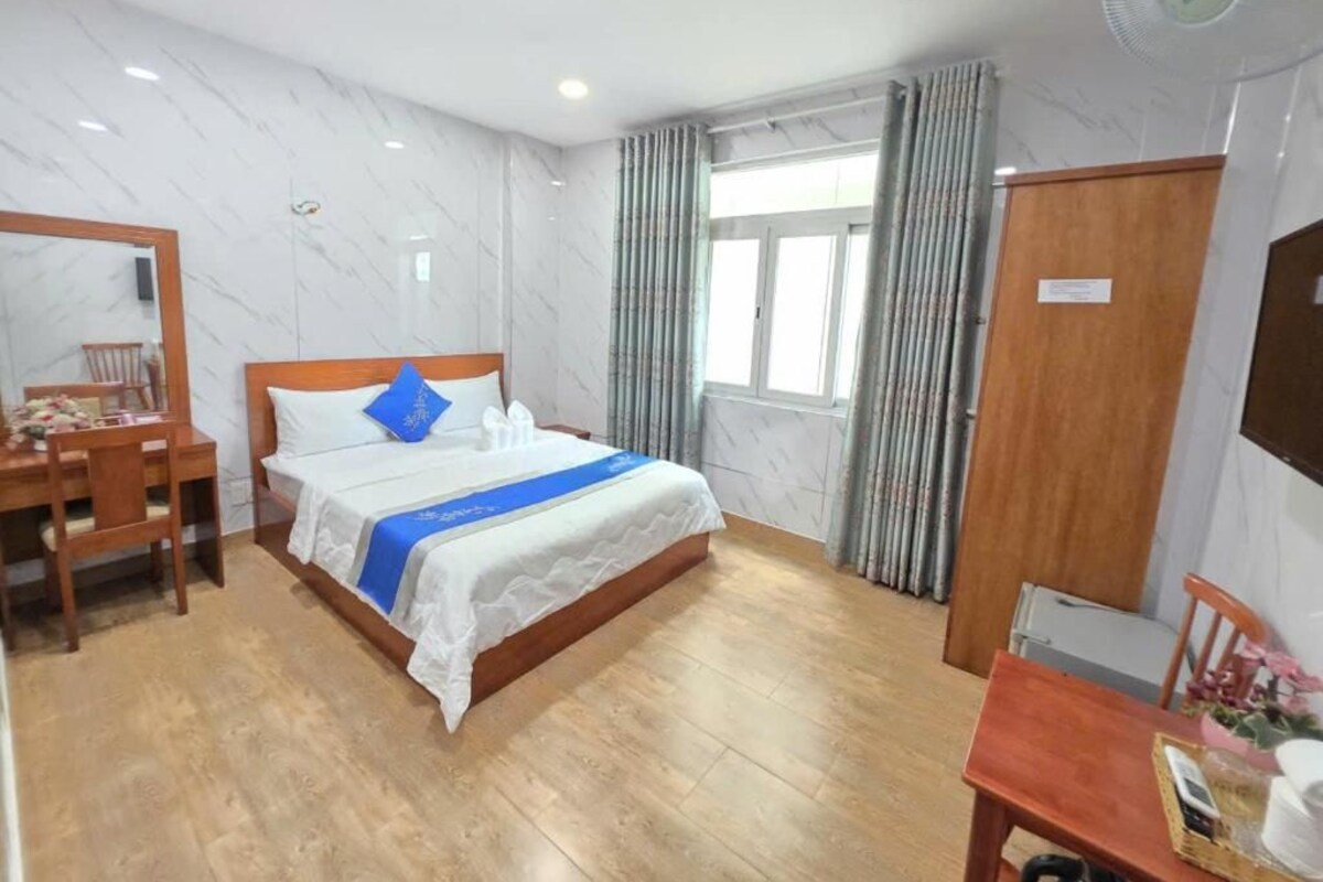 A hotel room with a bed, a desk, a chair, a wardrobe, and a window with curtains.