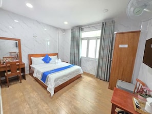 A hotel room with a bed, a desk, a chair, a wardrobe, and a window with curtains. - DŨNG INDIA HOTEL (Tân Bình)