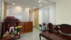 A lobby with a reception desk, a wooden cabinet with flowers, a fan, and a bench. - DŨNG INDIA HOTEL (Tân Bình)
