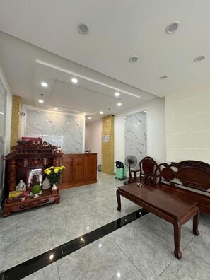 A lobby with a reception desk, a wooden cabinet with flowers, a fan, and a bench. - DŨNG INDIA HOTEL (Tân Bình)