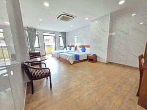 A hotel room with a large bed, a sitting area with a chair, a small table, and a bedside table. - Dũng India Hotel (Tân Bình)
