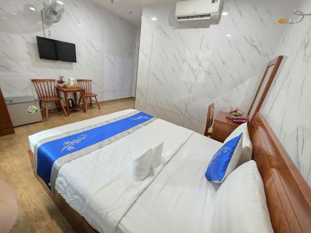 A hotel room with a bed, a desk, a chair, a television, and an air conditioning unit.
