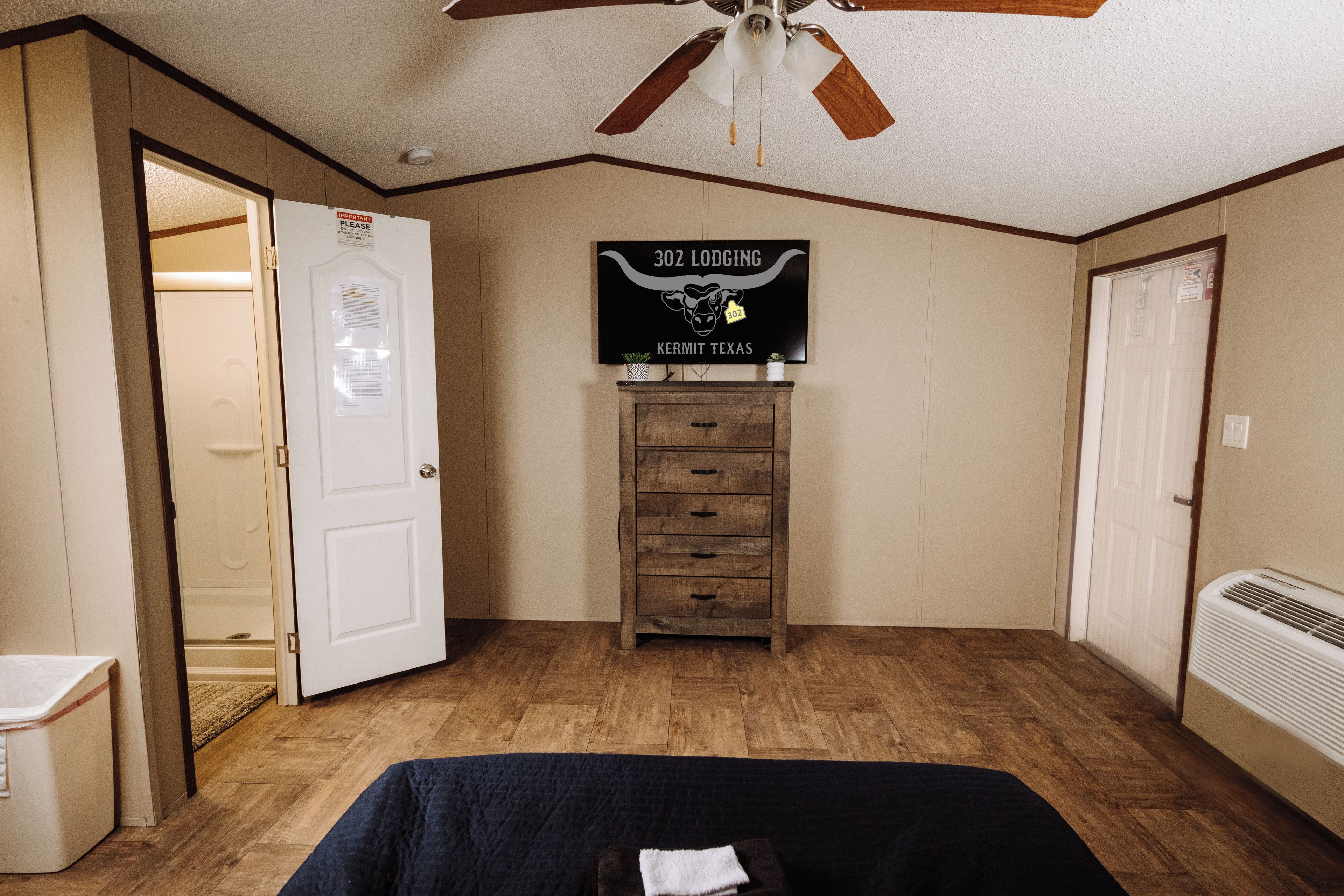 A bedroom with a bed, a ceiling fan, a dresser, and a sign on the wall.