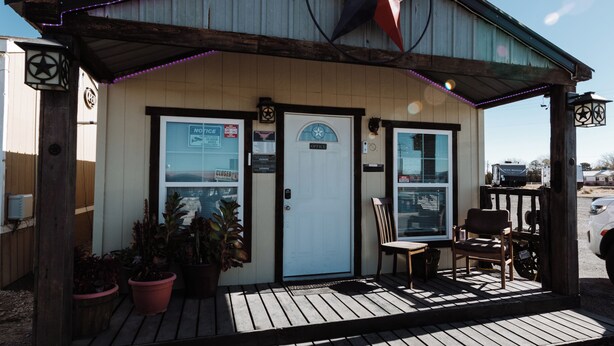 A small building with a closed office sign, a wooden porch with potted plants, and a chair. - 302 Lodging (Kermit)