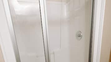 A glass-enclosed shower stall with a white frame, a visible drain, and a wooden floor.