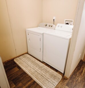 A laundry room with a front-loading washer and dryer, a wooden floor, and a beige rug.