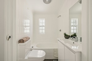 A bathroom with a bathtub, a toilet, a sink, and a mirror. - Charming 4BR Surry Hills Terrace Walk to CBD (Surry Hills)