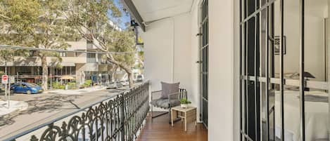 A balcony with a wooden floor, a chair, and a table with a plant.