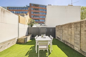 A patio with a table and chairs, surrounded by a low wall and a building in the background. - Charming 4BR Surry Hills Terrace Walk to CBD (Surry Hills)
