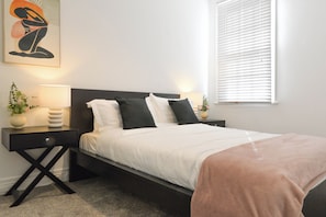 A neatly made bed with white bedding and a pink throw, flanked by two bedside lamps and a small table with a vase of flowers. - Charming 4BR Surry Hills Terrace Walk to CBD (Surry Hills)