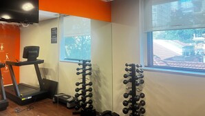 A gym with a treadmill, weight racks, and a window with a view of a building. - Cozy 1-bedroom bed & breakfast in peaceful São Paulo with AC (São Paulo)