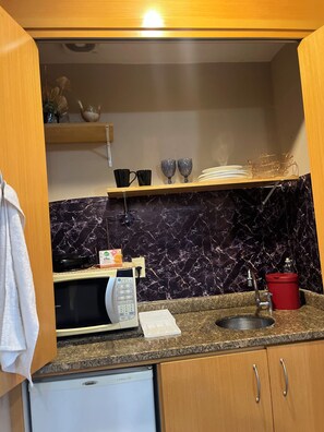 Pieni, käytännöllinen keittiö, jossa on mikroaaltouuni, pesuallas ja puukehikoiset kaapit.