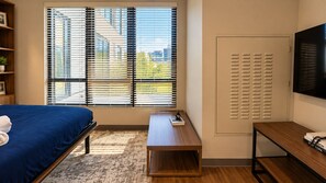 A bedroom with a bed, a desk, a TV, and a window with blinds. - Stylish Studio with Birmingham City Views C1 (Birmingham)