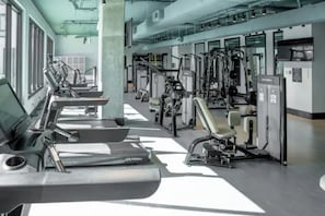 Ein Fitnessstudio mit verschiedenen Trainingsgeräten, darunter Laufbänder und Gewichte, die in Reihen angeordnet sind.