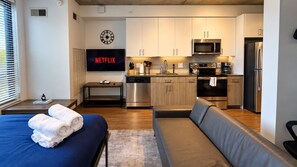 Ein modernes Hotelzimmer mit Bett, einer Couch, einer Küchenzeile und einem Flachbildfernseher, der das Netflix-Logo zeigt.