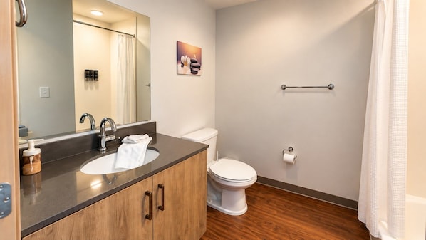 Ein Badezimmer mit einem Holzbadezimmer-Möbel, einem Waschbecken, einer Toilette und einer Duschvorhang.