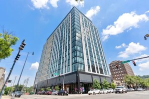 A tall, modern building with a glass facade, located at a street corner with traffic lights and cars. - Stylish Studio with Birmingham City Views B1 (Birmingham)