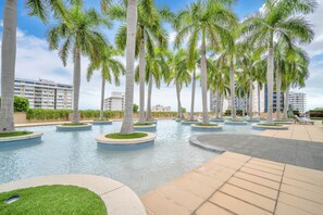 Área de piscina com palmeiras e um edifício ao fundo.