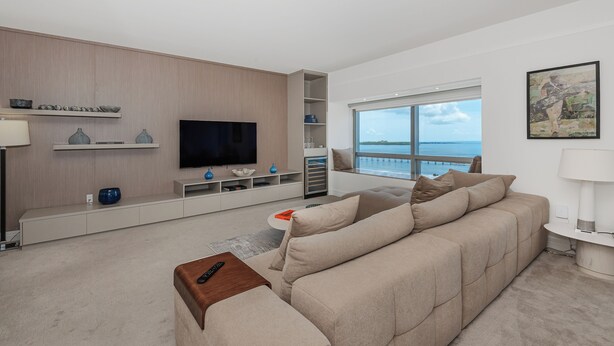 A modern living room with a large flat-screen TV, a beige sofa, a coffee table, and a view of the sea through a large window. - Luxury Four seasons Hotel Miami 2 Bedroom Oceanview Luxury Suite. (Miami)