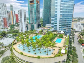 Um edifício alto com piscina no terraço, rodeado por palmeiras.
