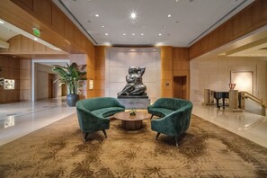 Um saguão com dois poltronas verdes, uma escultura central e um tapete estampado.