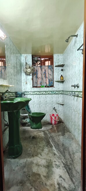 A bathroom with a green sink, a toilet, a shower, and a window with a floral curtain. - Mudiali Haven: A peaceful 2BHK in South Kolkata - near Kalighat Metro (Kolkata)