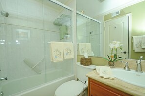 Casa de banho com cabine de duche em vidro, sanita, lavatório com espelho e toalhas.