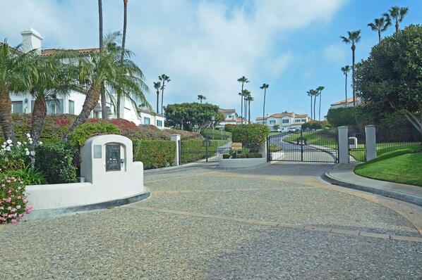 Uma entrada com portão leva a um bairro residencial com palmeiras e casas.