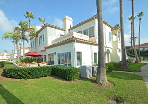 Uma casa de dois andares com fachada branca, telhado de telhas vermelhas e varanda coberta com um guarda-sol vermelho.