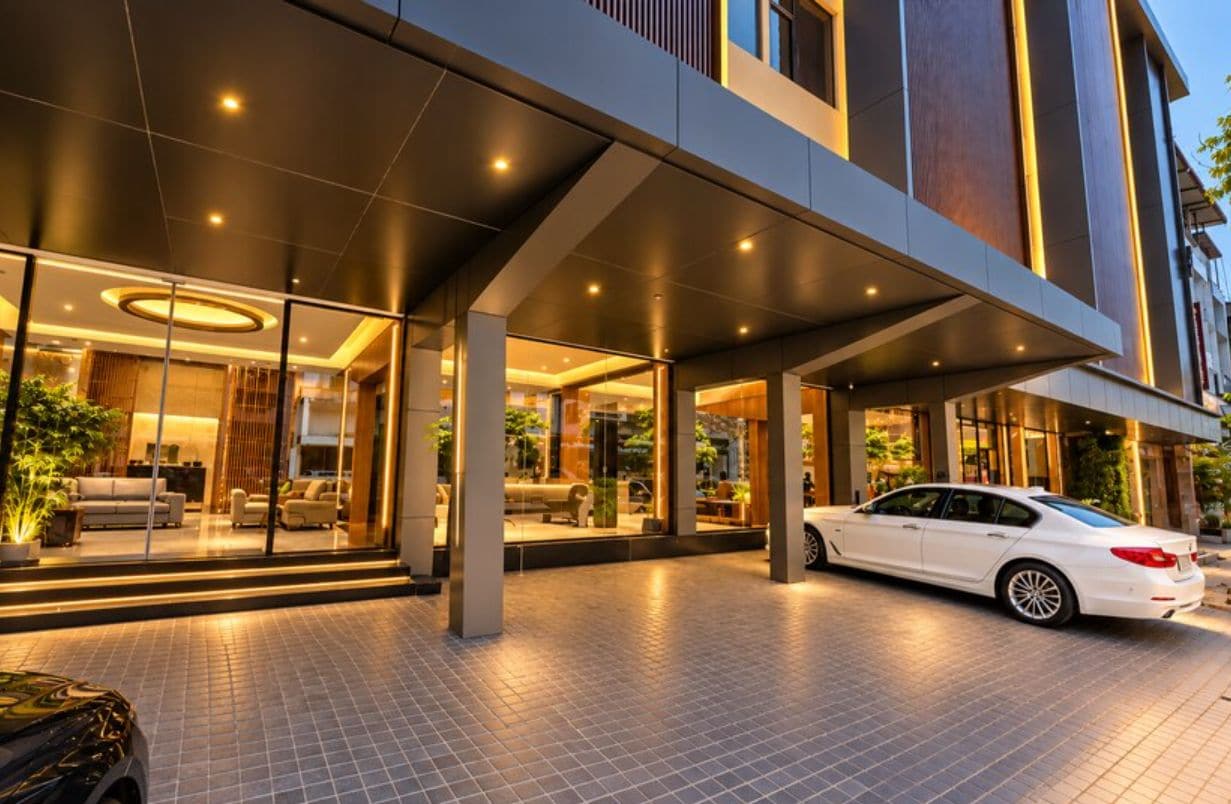 Ein moderner Hotel Eingangsbereich mit überdachtem Außenbereich, einem weißen Auto vor der Fassade und einer Glasfront.