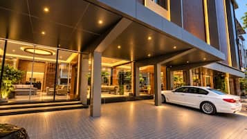 Una entrada de hotel moderna con un espacio exterior cubierto, un coche blanco estacionado al frente y fachada de vidrio.