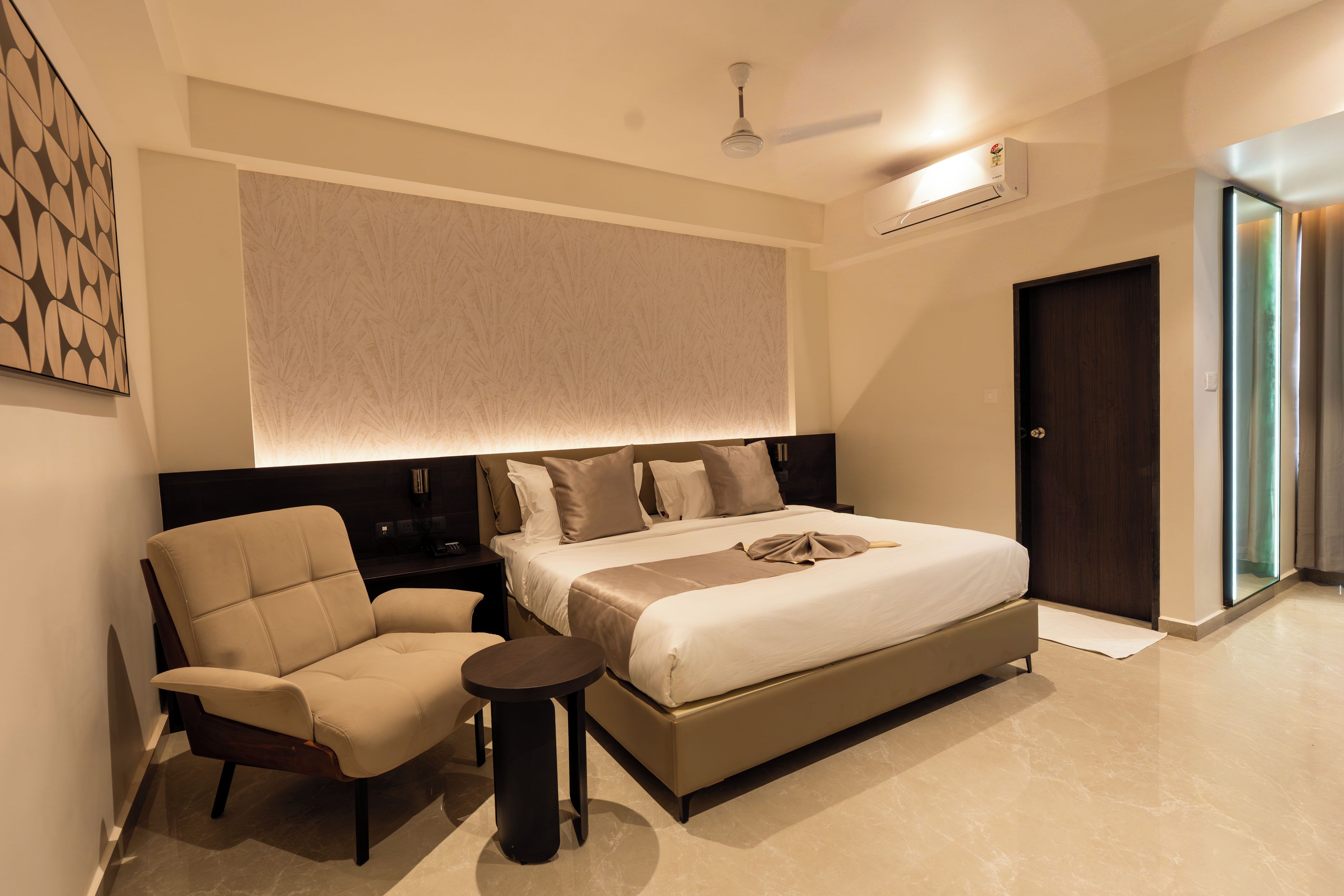 A modern hotel room with a large bed, a seating area with a chair, a bedside table, and a ceiling fan.