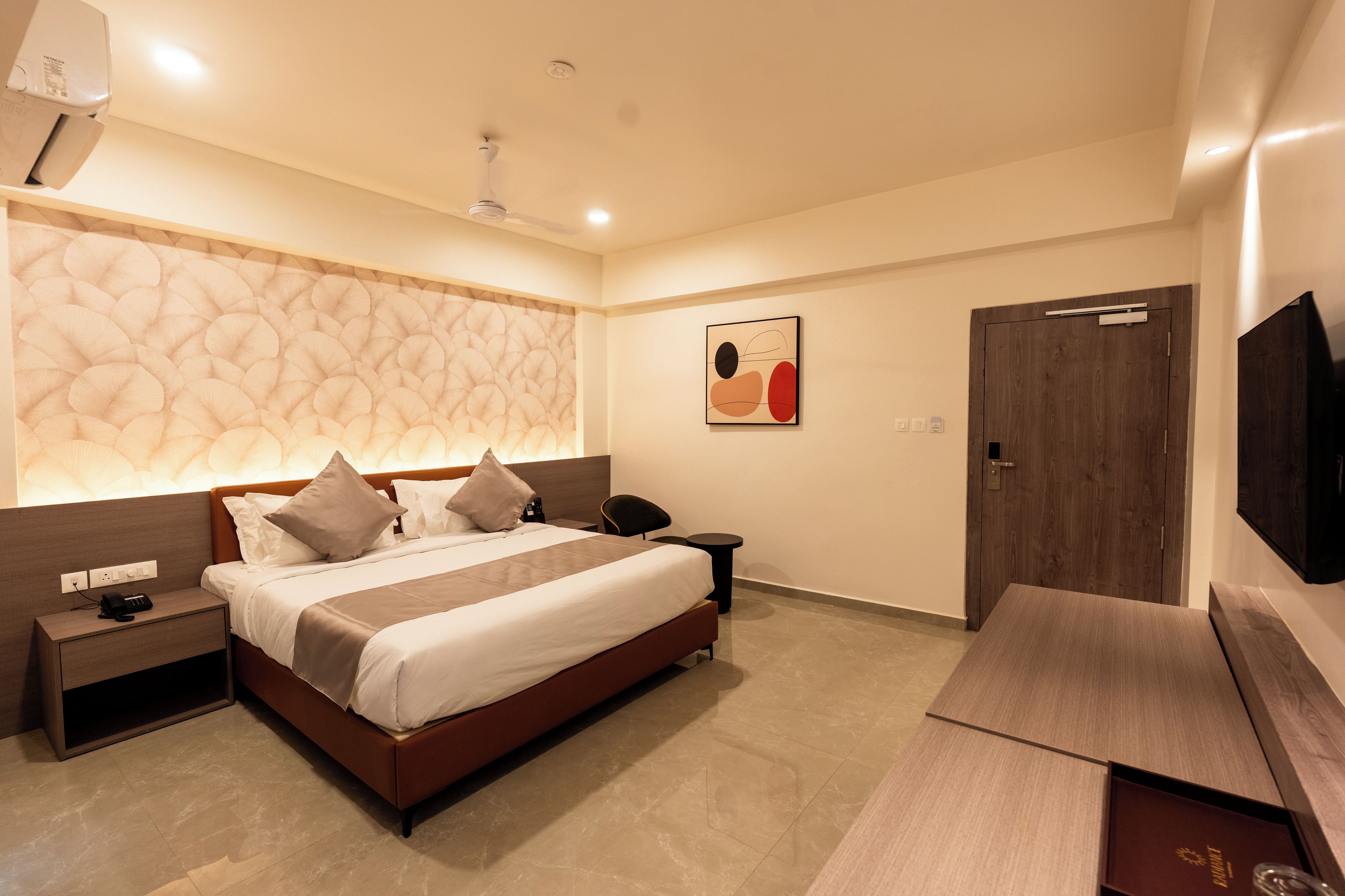 A modern hotel room with a large bed, bedside tables, a flat-screen TV, and a decorative wall panel.