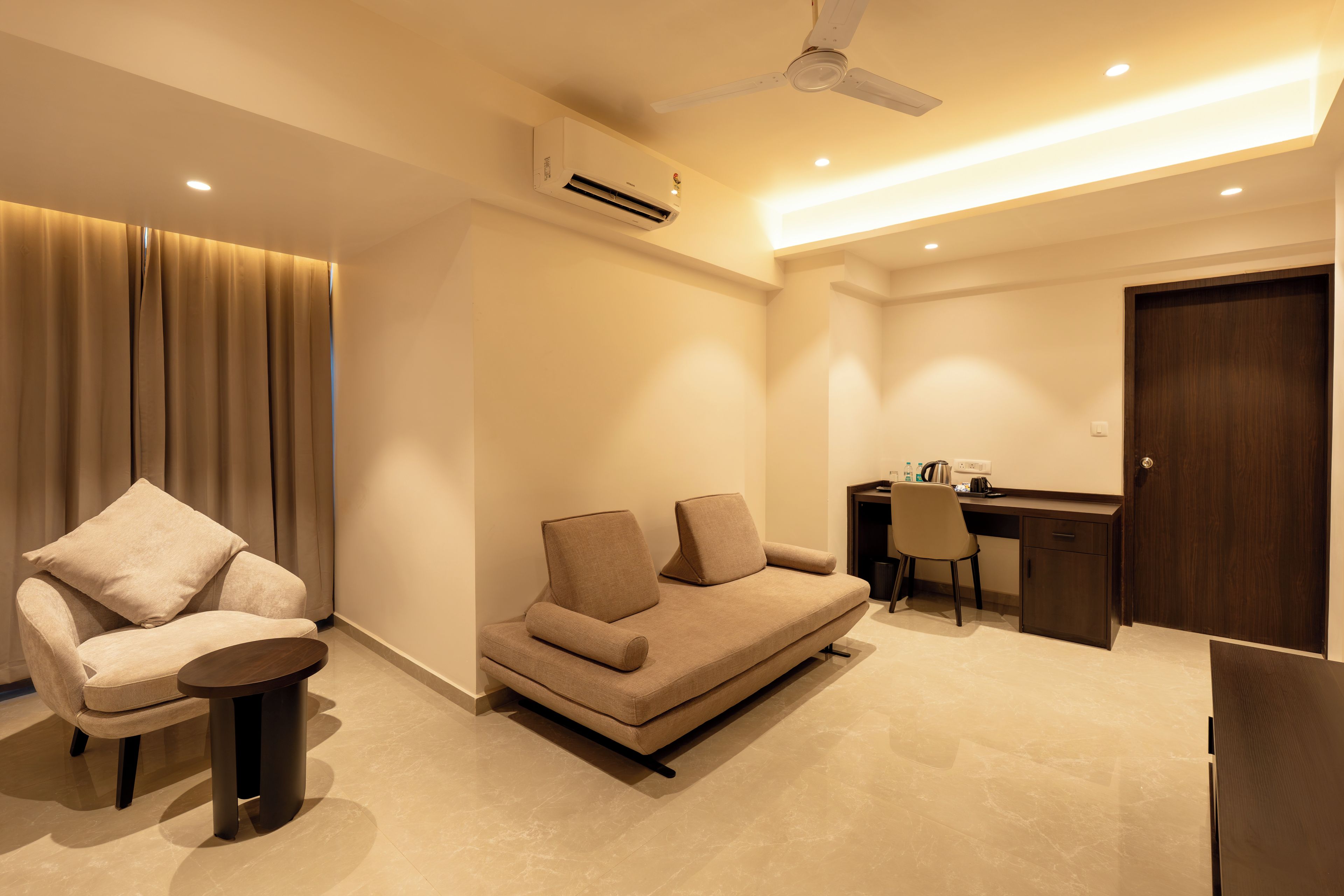 A modern living room with a sofa, a chair, a small table, a desk, and a ceiling fan.