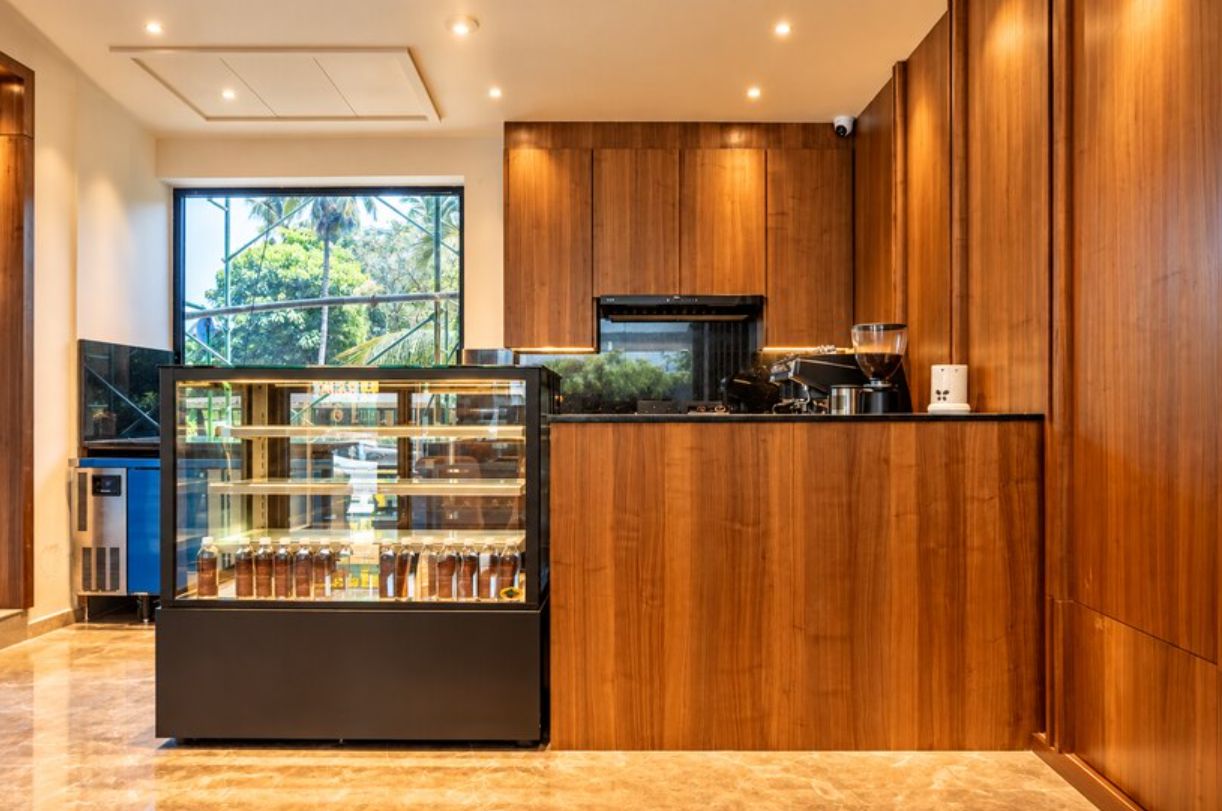 A modern kitchen with wooden cabinets, a coffee machine, and a display case with bottles.