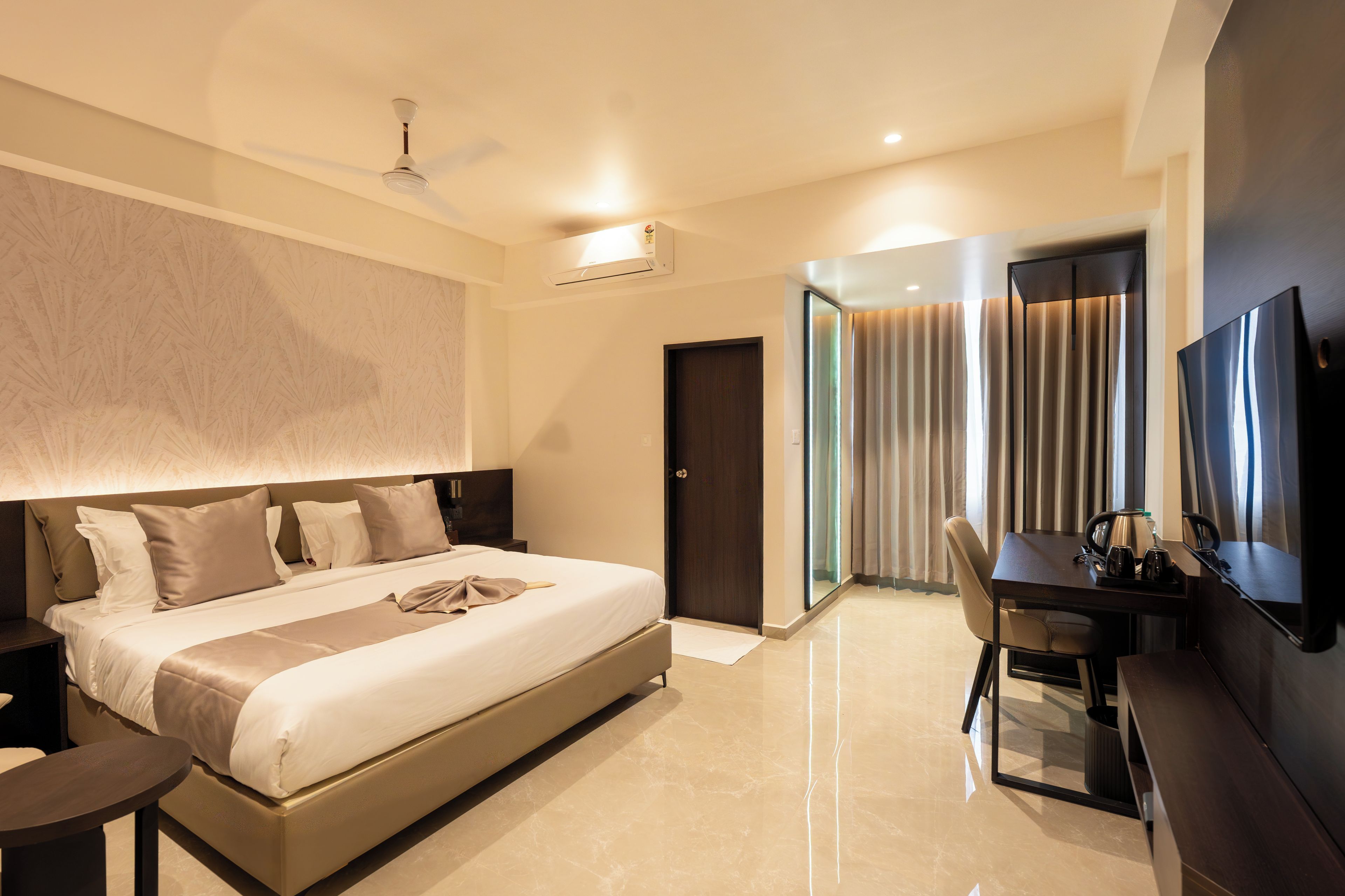A modern hotel room with a large bed, a desk, a chair, a flat-screen TV, and a ceiling fan.