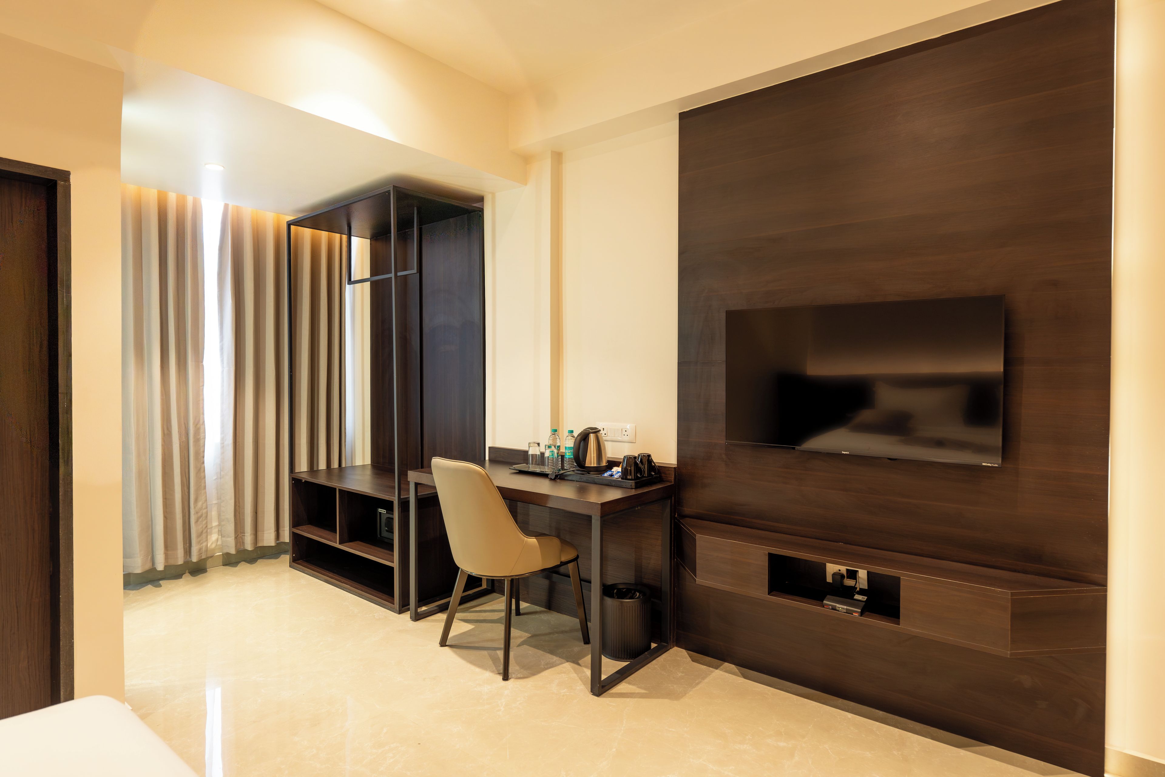 A hotel room with a dark wood panel wall, a flat-screen TV mounted on it, a desk with a chair, and a small trash bin.