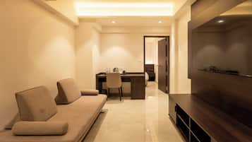 A modern hotel room with a sofa, a desk, and a large flat-screen TV.