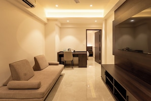 A modern hotel room with a sofa, a desk, and a large flat-screen TV.