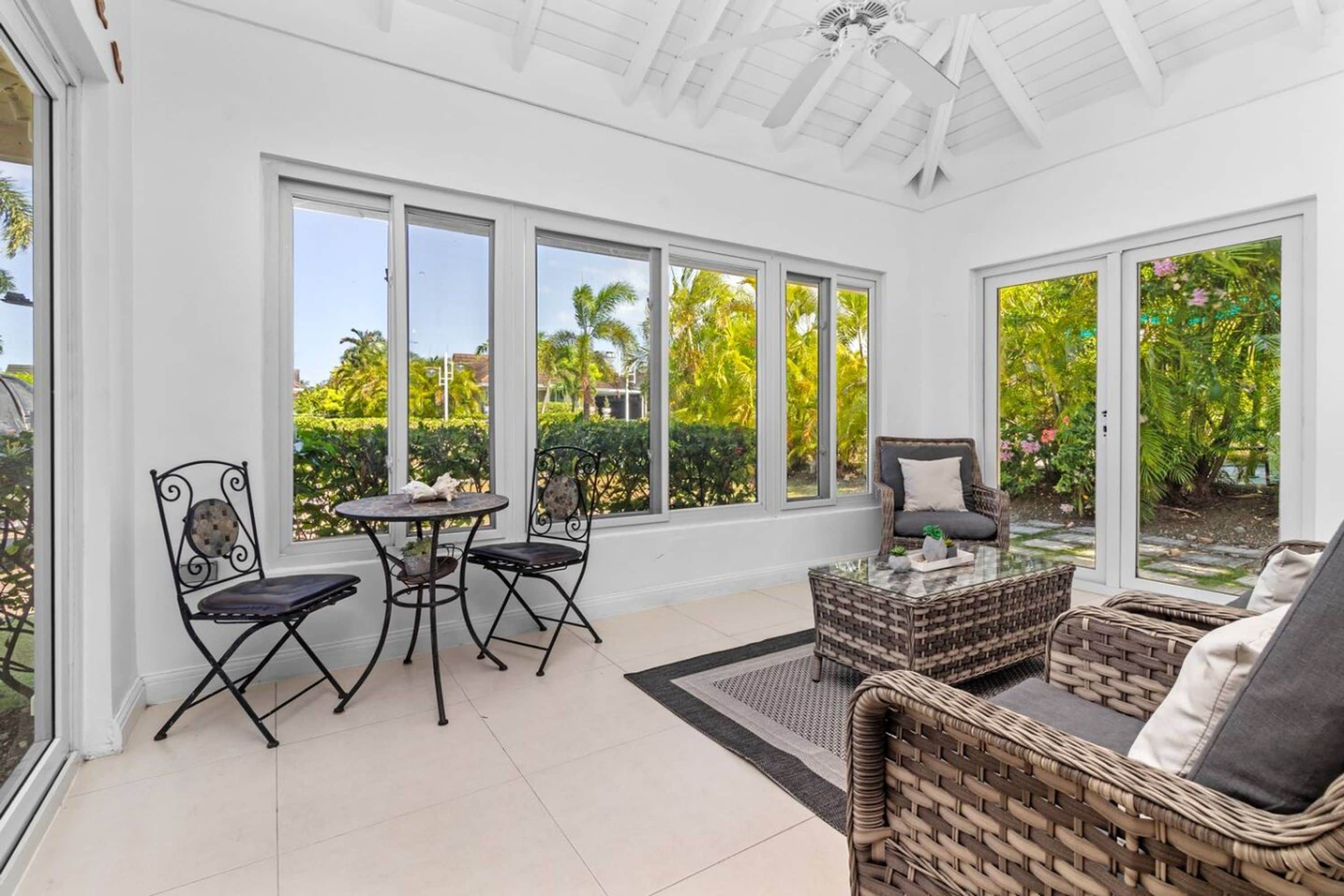 A conservatory with a glass ceiling, a wicker sofa, a round table, and two chairs.