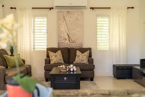 A living room with a sofa, coffee table, and a painting of a sailboat. - Richmond Retreat Pool Gym Gated Beach Access (St. Ann's Bay)