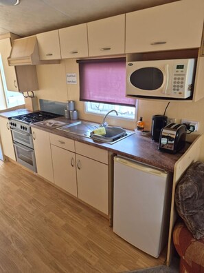 A compact kitchenette with a stove, microwave, sink, and a small refrigerator. - Cosy Caravan 2BR in Sandown Sleeps 4 With Free Parking (Sandown)