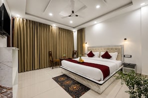 Habitación de hotel con una cama grande, ventilador de techo, televisor y minibar.