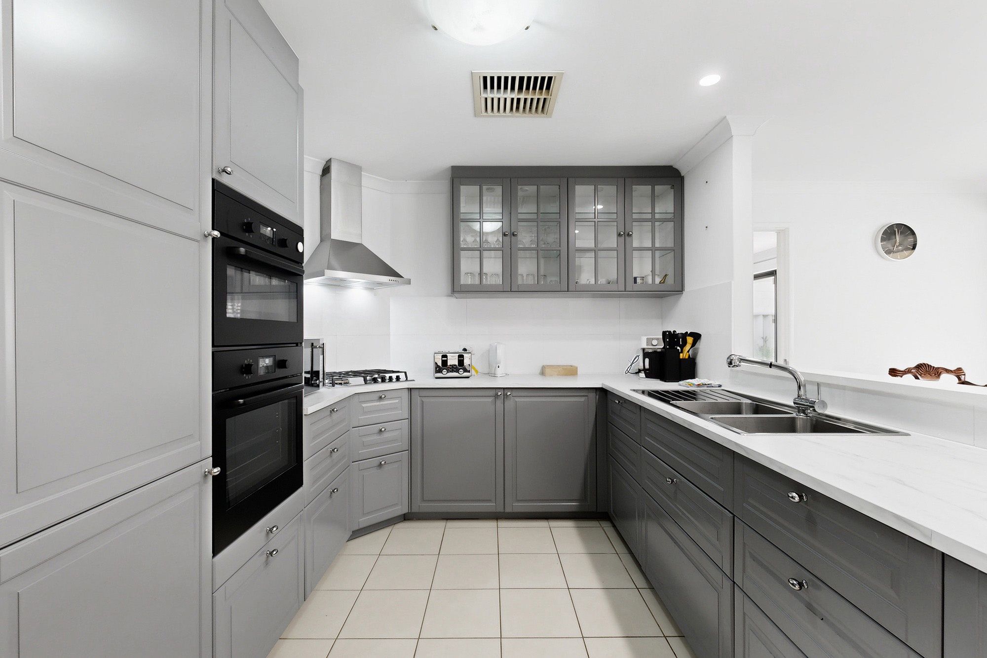 A modern kitchen with grey cabinets, a stainless steel sink, and a built-in oven.