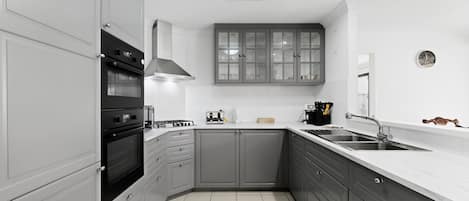A modern kitchen with grey cabinets, a stainless steel sink, and a built-in oven.