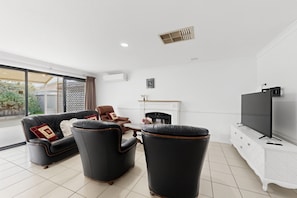 A modern living room with a black leather sofa, two armchairs, a flat-screen TV, and a fireplace. - Spacious 4-Bed House Near Mandurah (Dudley Park)