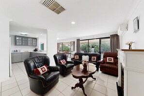 A modern living room with leather sofas, a wooden coffee table, and a view of the outdoors through large windows. - Spacious 4-Bed House Near Mandurah (Dudley Park)