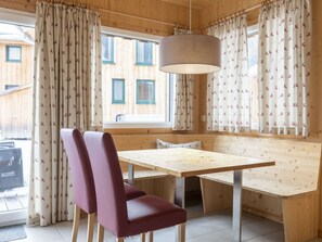 A wooden interior with a table and chairs, a hanging light fixture, and patterned curtains. - One-bedroom Cabin (Sankt Georgen am Kreischberg)