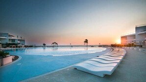 Una piscina a bordo curvo, una zona relax con panche bianche e vista sull'oceano al tramonto.