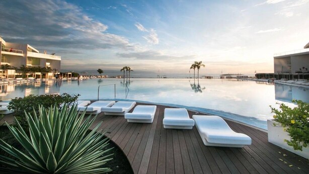 Una piscina di un resort con lettini, palme e cielo sereno.